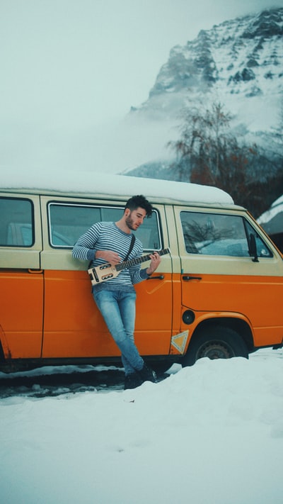 男人倚在车旁,蓝天下弹吉他
